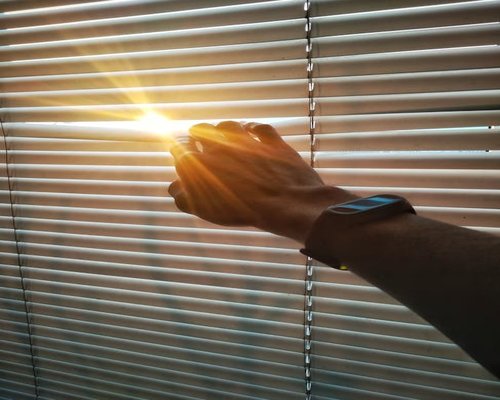 Person adjusting blinds to reduce glare on computer